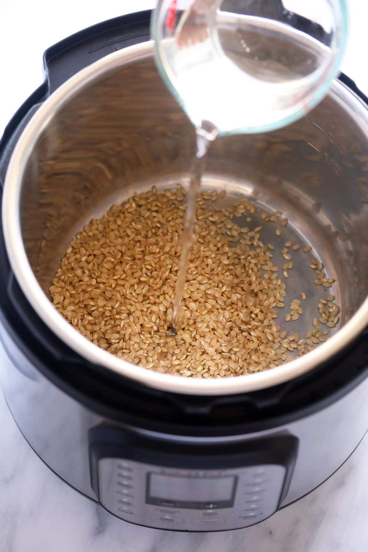 Pouring water into the Instant Pot with the brown rice. 