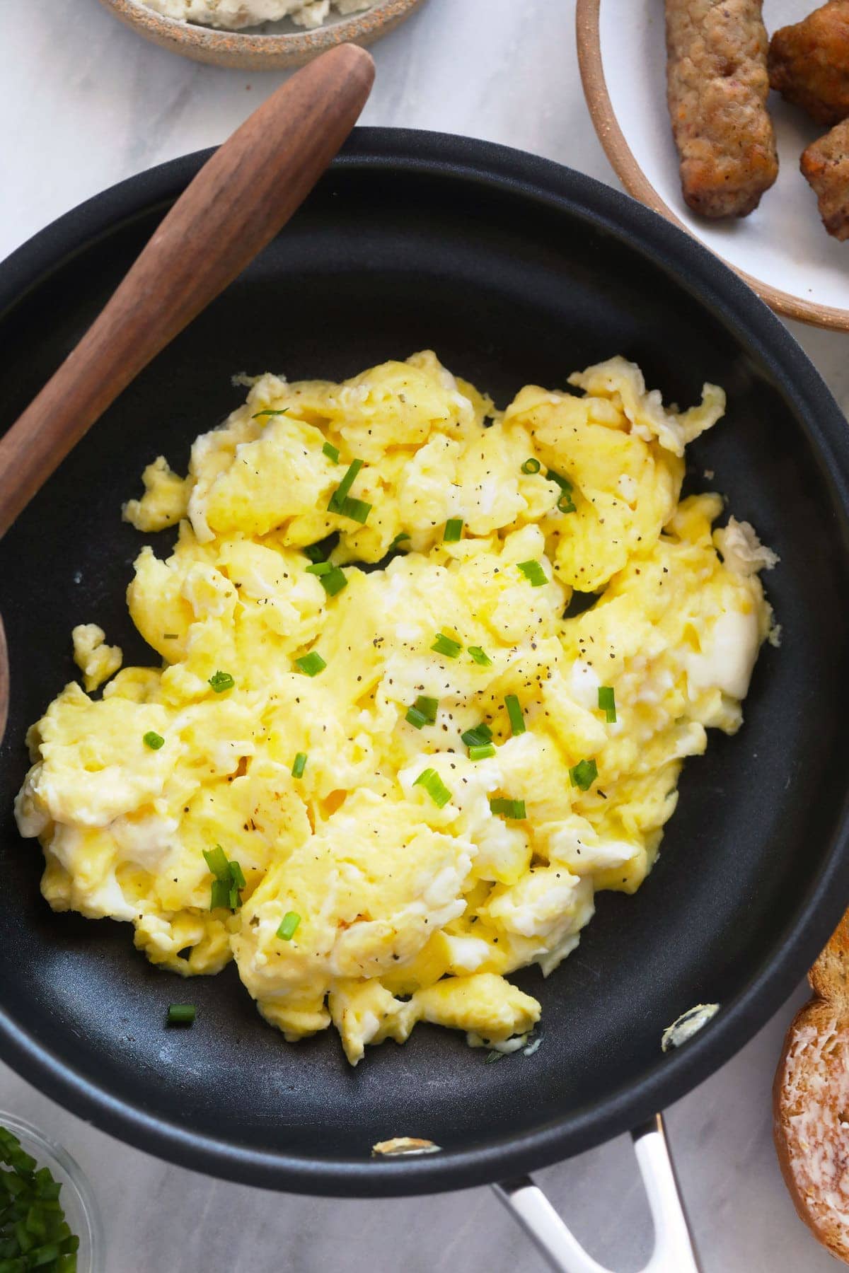 perfect scrambled eggs in a skillet topped with chopped chives