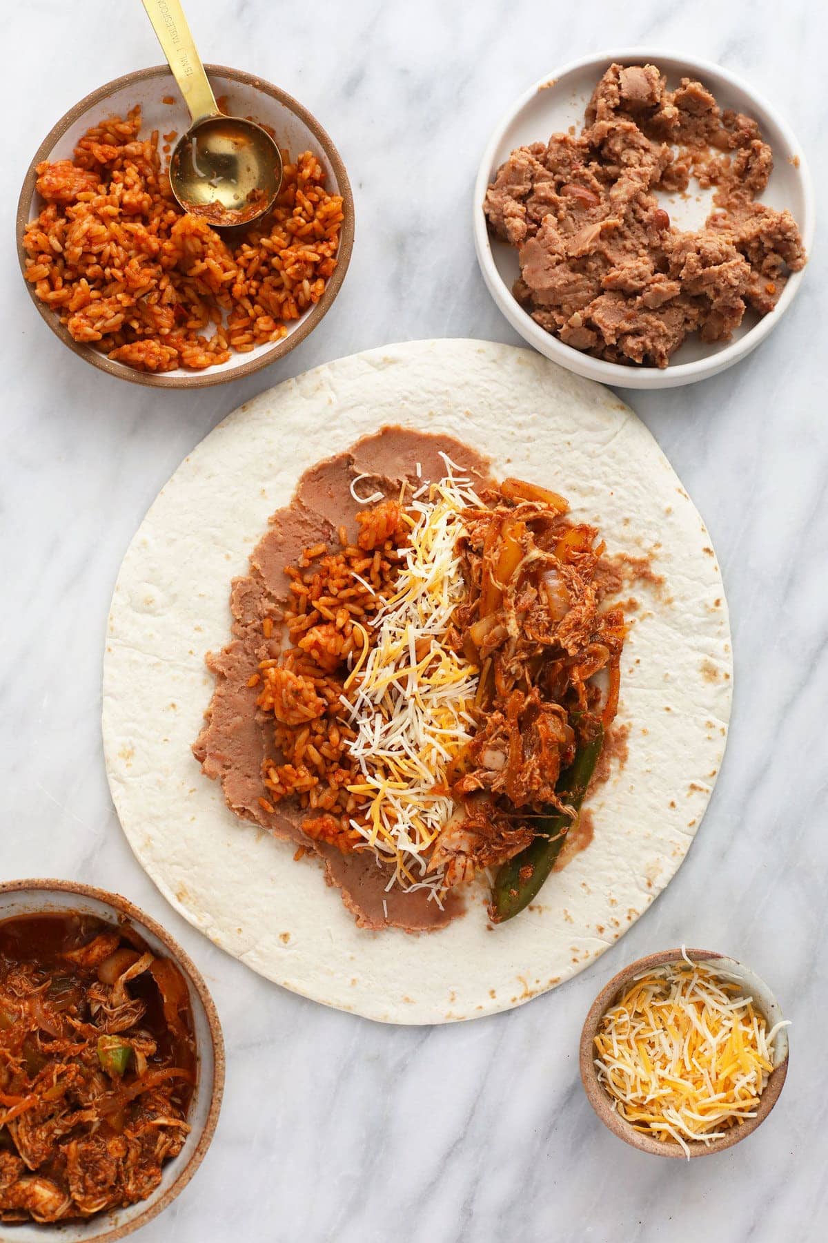 shredded chicken burrito ingredients being assembled onto a flour tortilla.