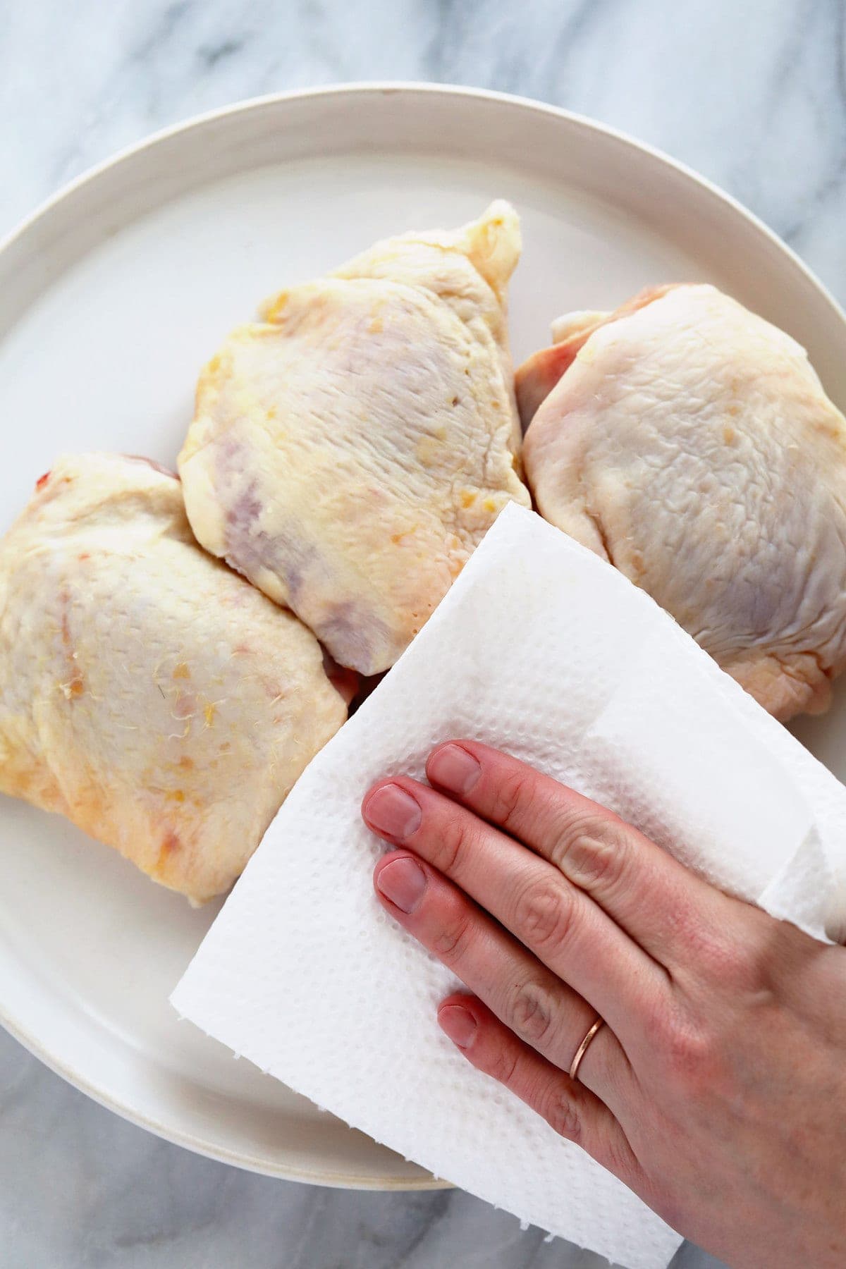 Removing moisture from the chicken thighs with a paper towel. 