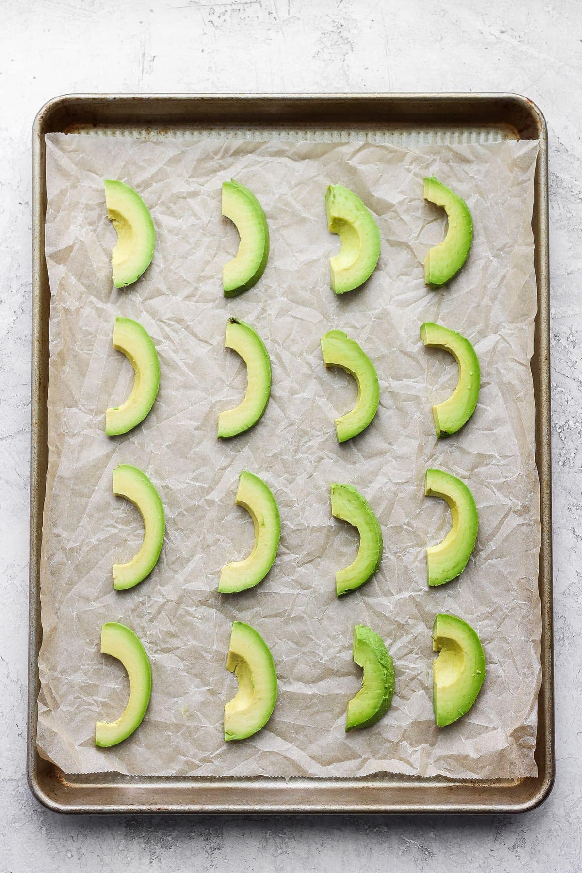 slices of avocado on parchment paper and a baking sheet, ready to be placed in the freezer