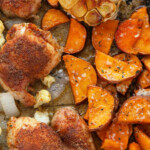 Chicken thighs, sweet potatoes, and cauliflower on a baking sheet.