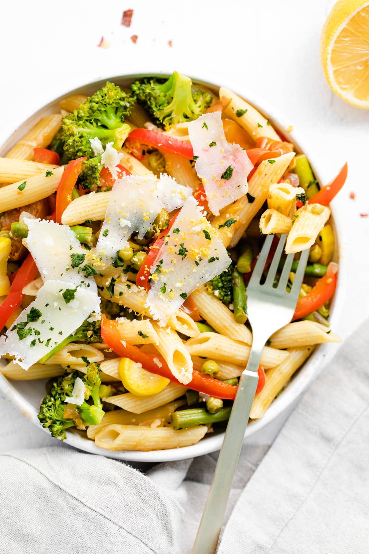 pasta primavera in a bowl topped with parmesan cheese and fresh basil