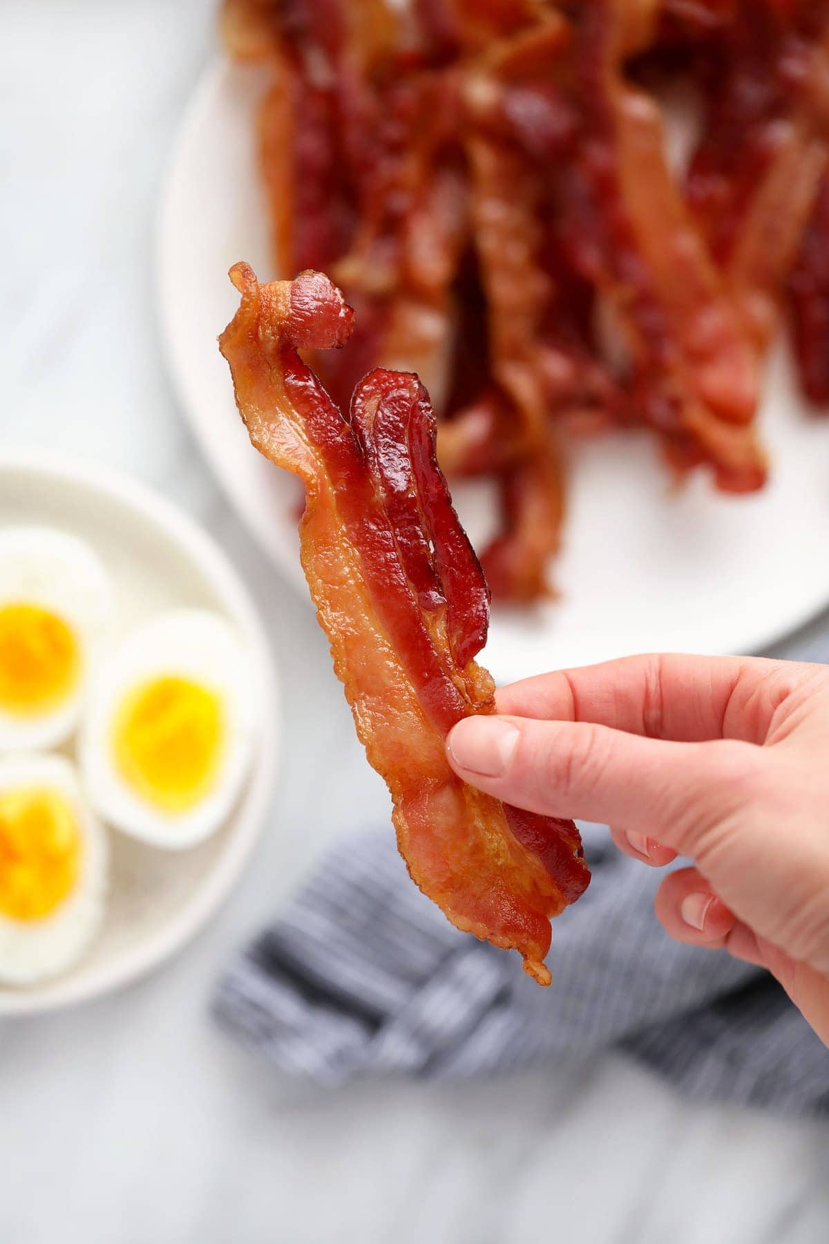 A hand holding a piece of bacon. 