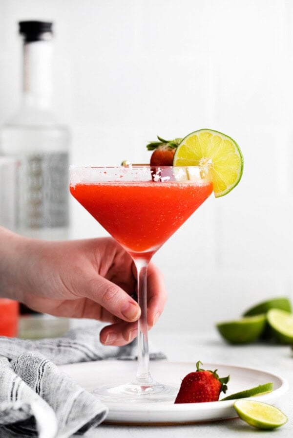 a person holding a strawberry margarita on a plate.