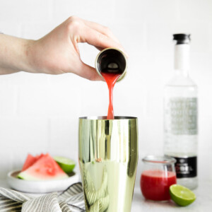 a person pouring watermelon juice into a gold cup.