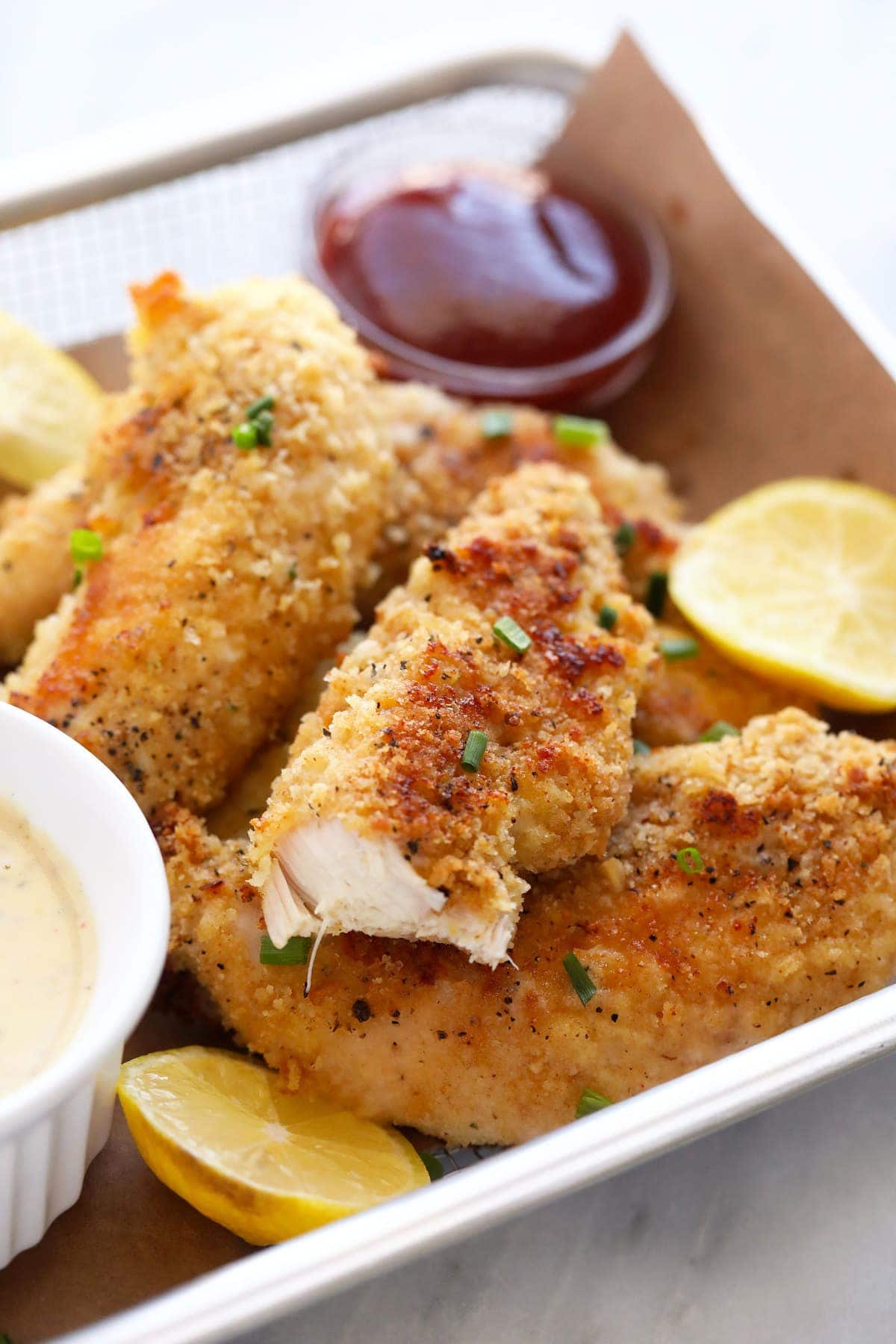 Chicken tenders in a basket with ketchup, lemons, and honey mustard. 