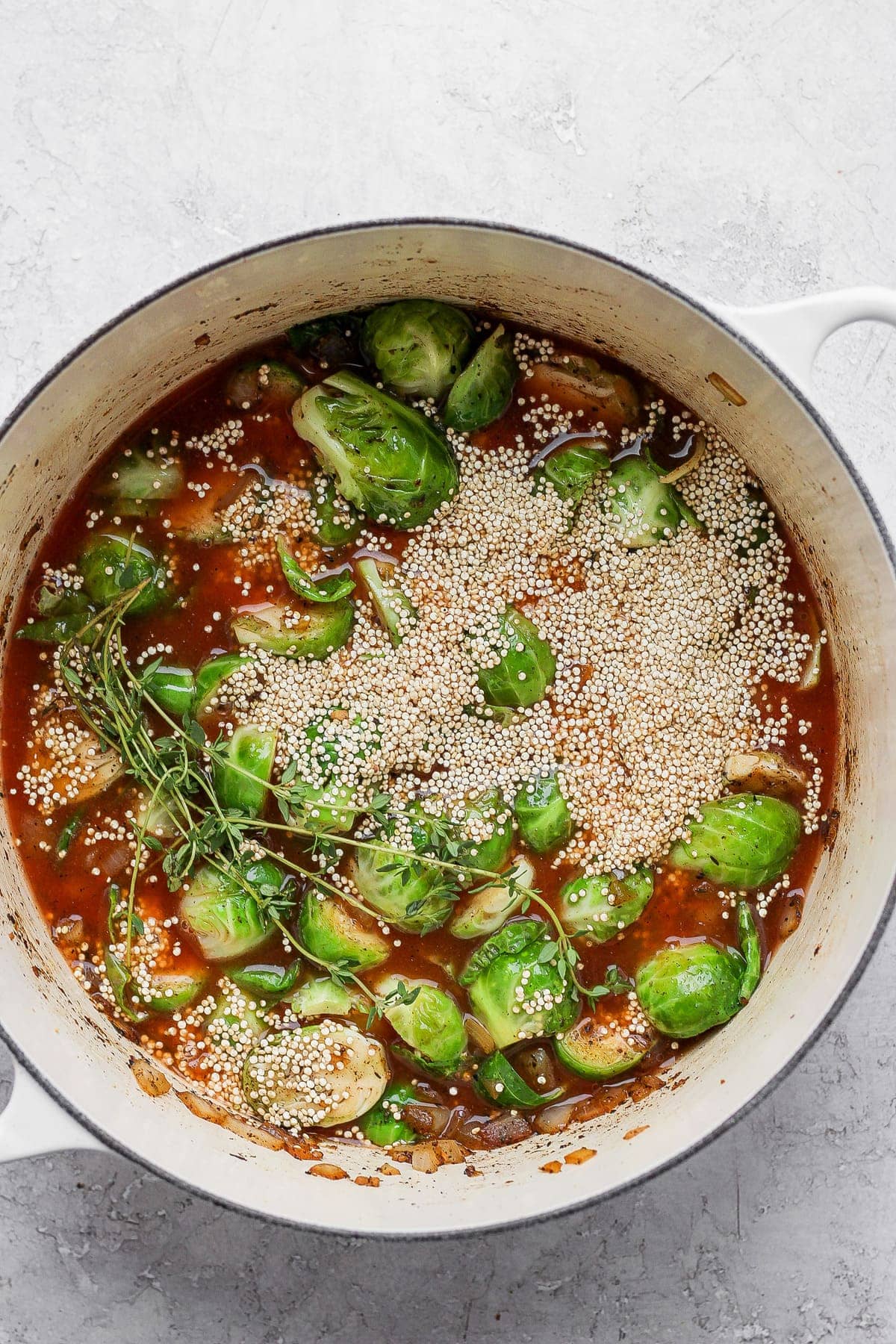 Brussels sprouts, uncooked quinoa, and broth in Dutch oven