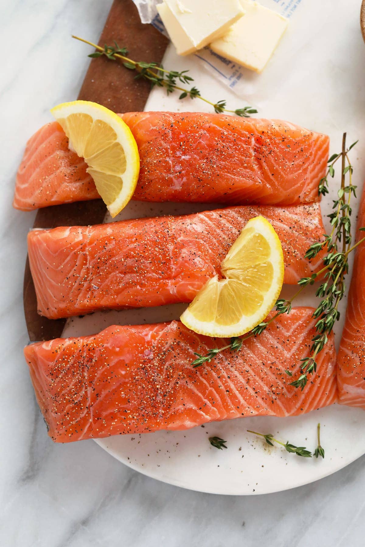 Raw salmon with salt, pepper, fresh lemon, and thyme on a plate. 