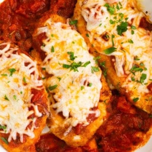 chicken breasts in a white dish with sauce and cheese.