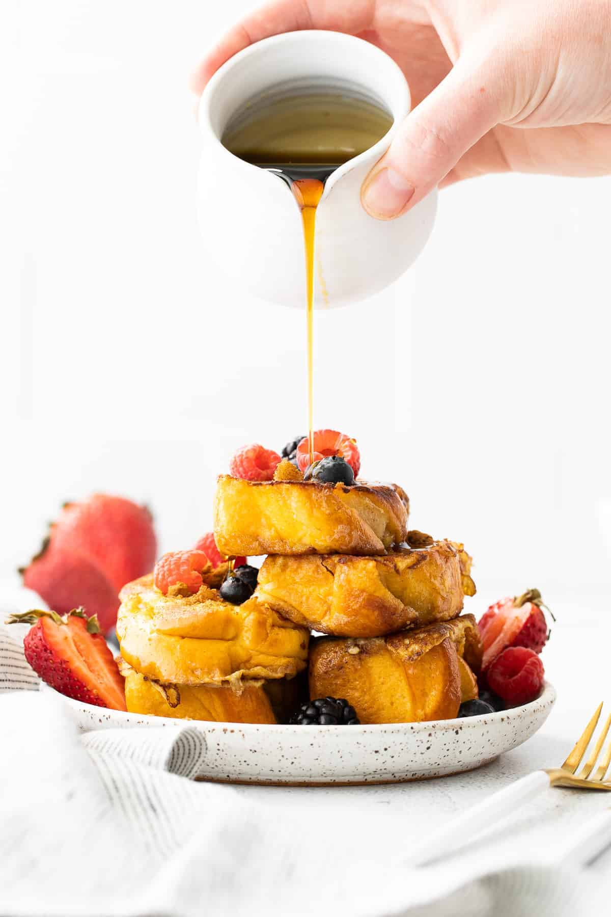 maple syrup being poured over slices of french toast topped with berries