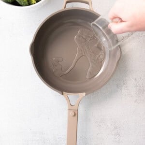 a person pouring water into a frying pan.