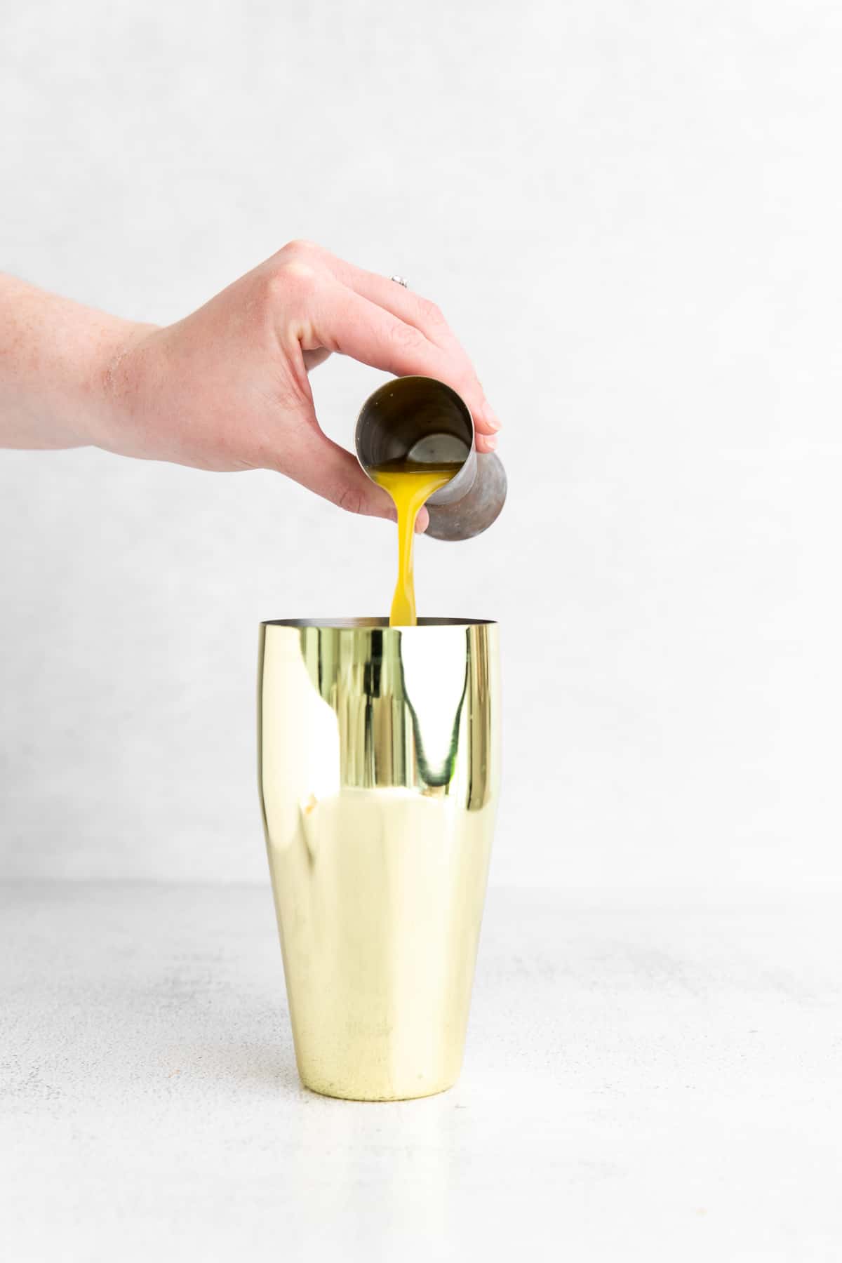 pouring orange juice into a cocktail shaker.