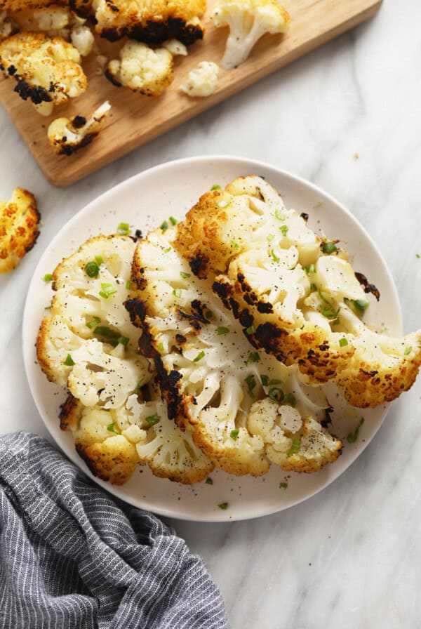 a white plate topped with cauliflower next to a cutting board.