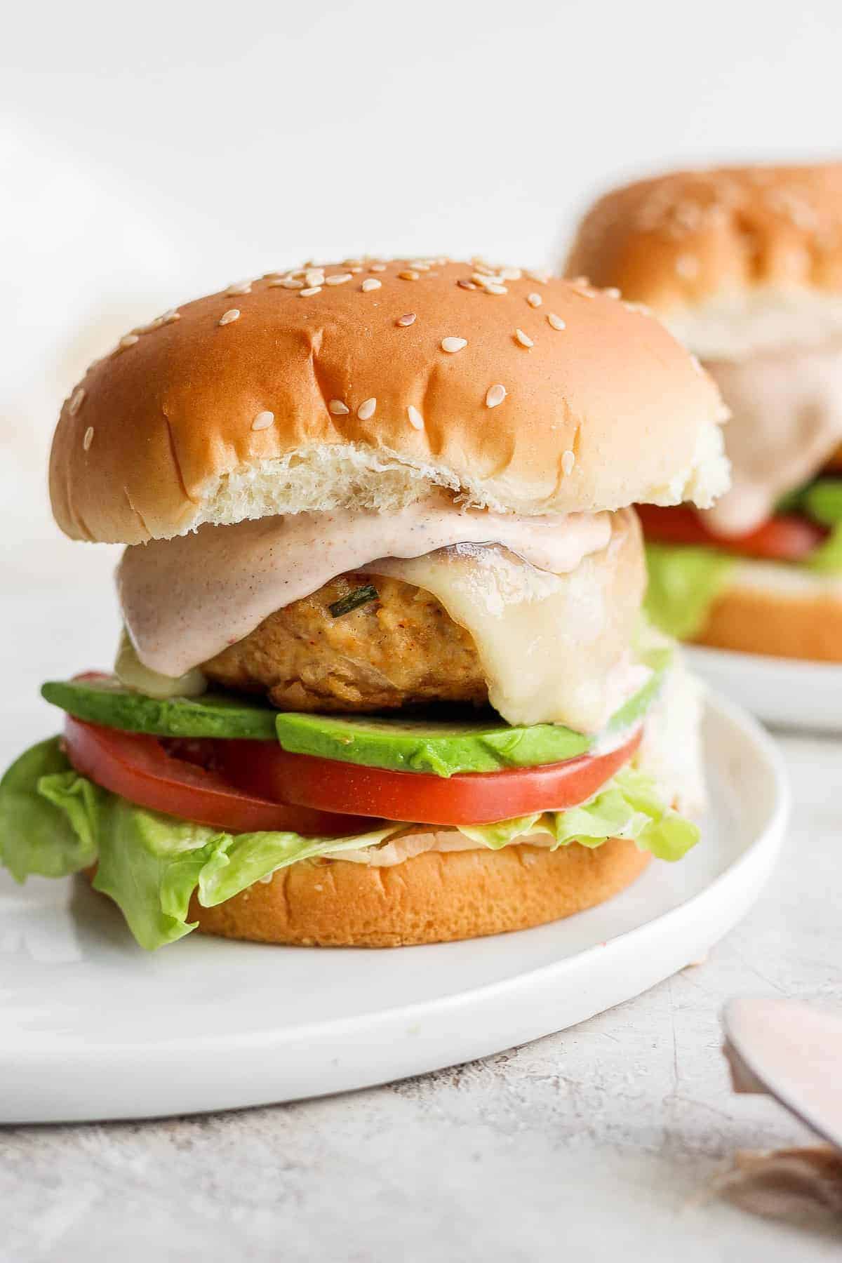 chicken burger on bun with avocado and tomato.