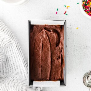 A box of chocolate ice cream with sprinkles and a spoon.