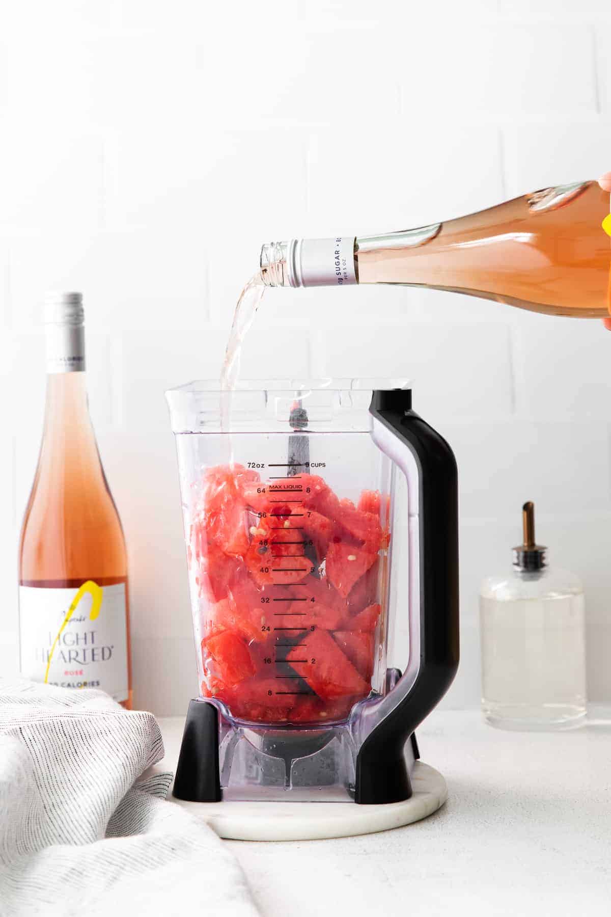 pouring a bottle of rosé into a blender with frozen watermelon