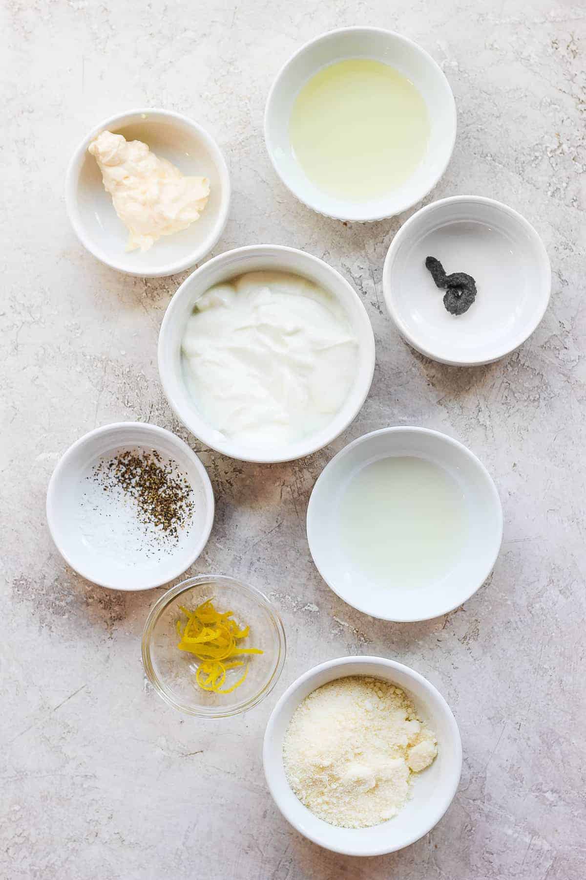 All of the ingredients for caesar salad dressing in small bowls. 