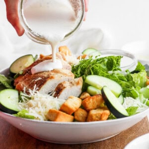 Pouring caesar dressing over a salad.