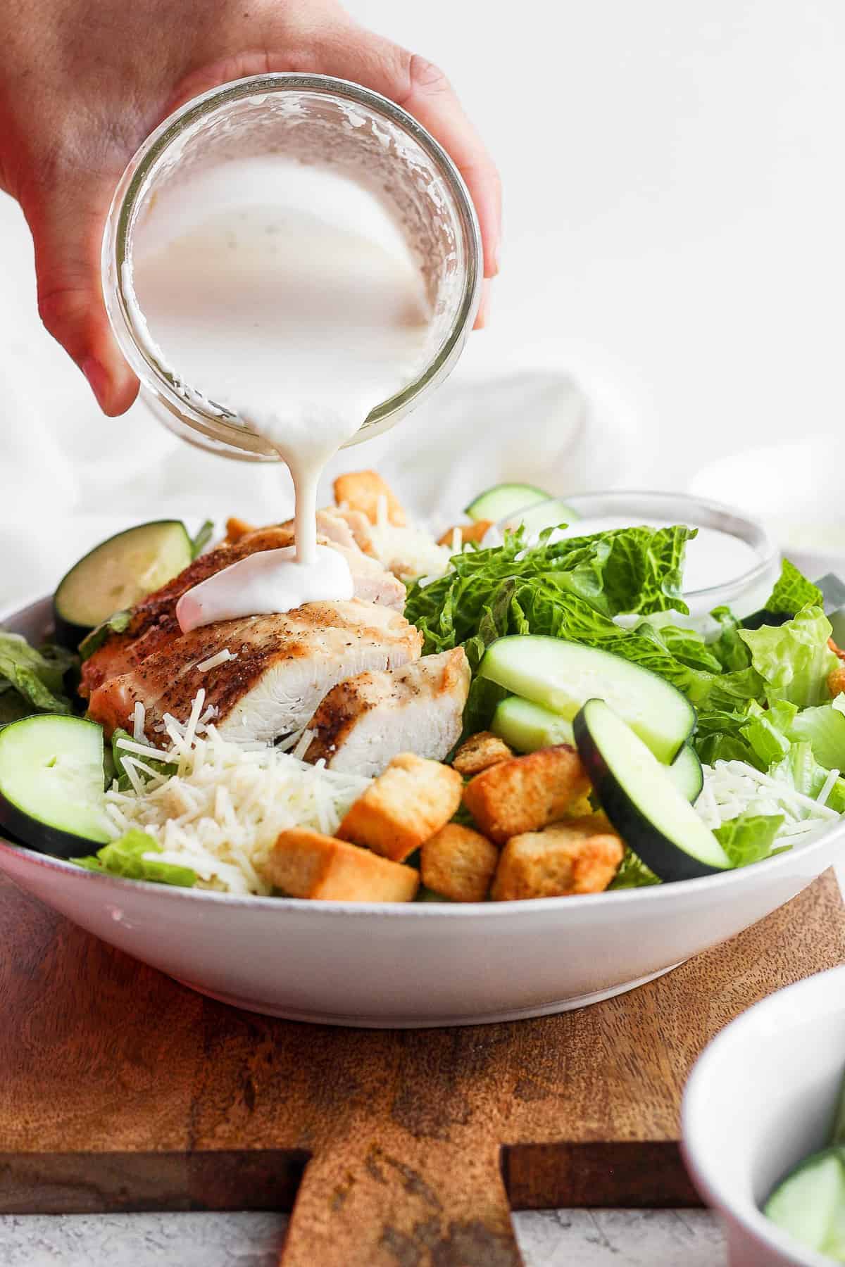 Pouring caesar dressing over chicken caesar salad. 