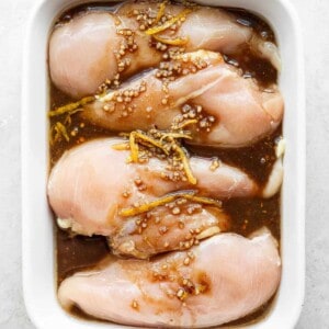 raw chicken in a white casserole dish with sesame seeds.