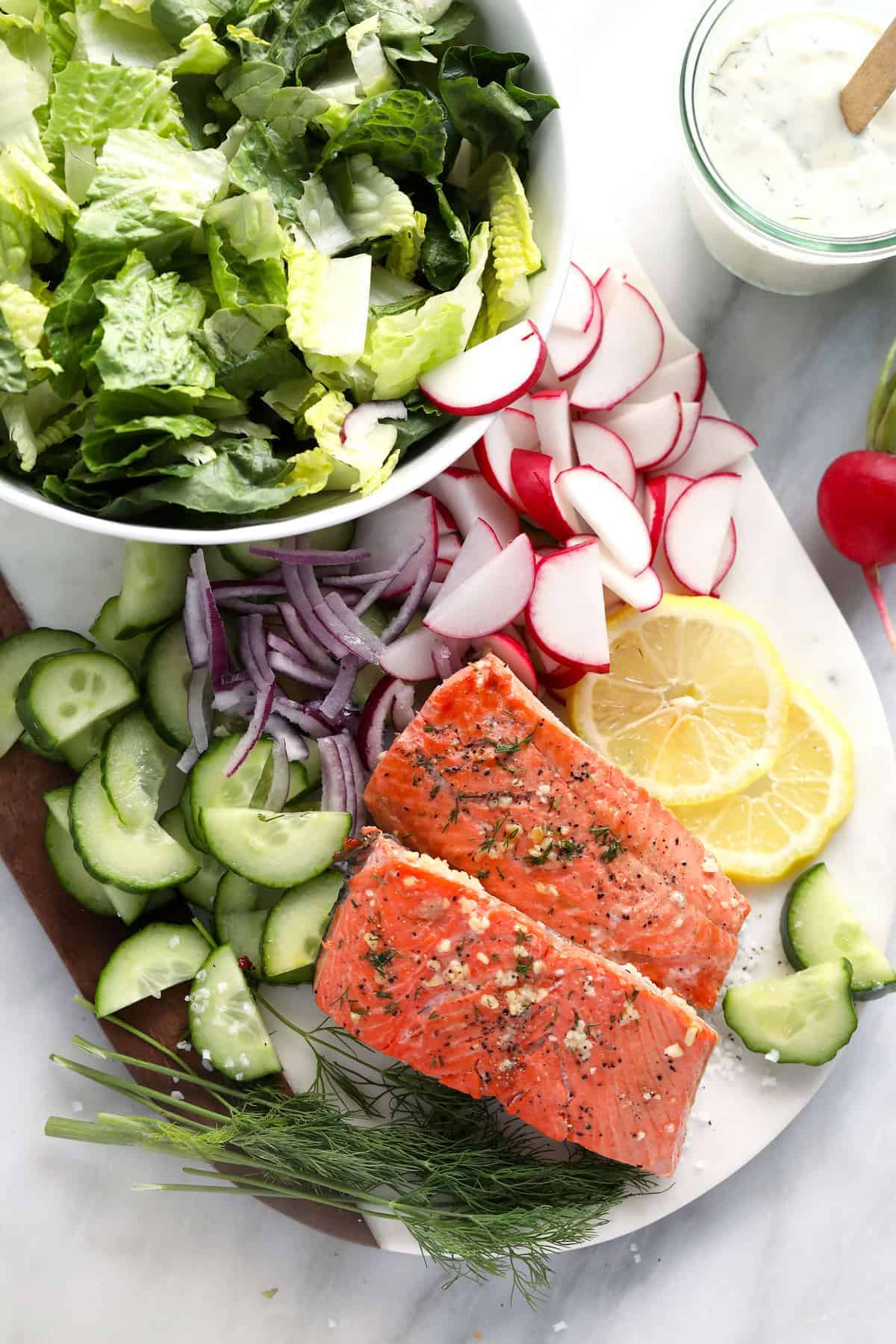 Veggies, lemon, and cooked salmon in cutting board.