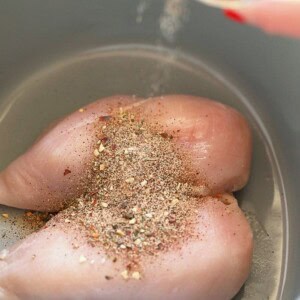 A person is seasoning and slow cooking chicken in a slow cooker for pulled chicken.