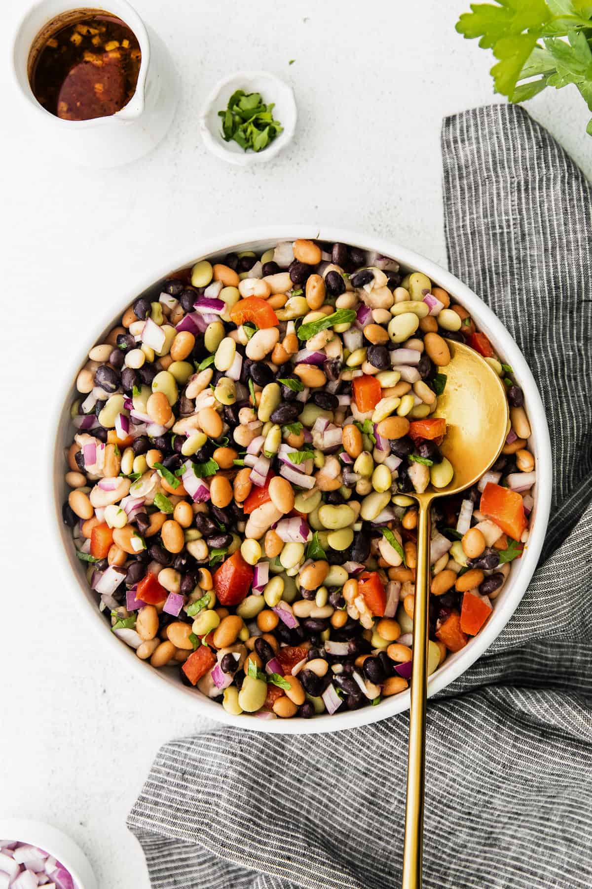 Bean salad in a bowl with dressing and fresh herbs on the side. 