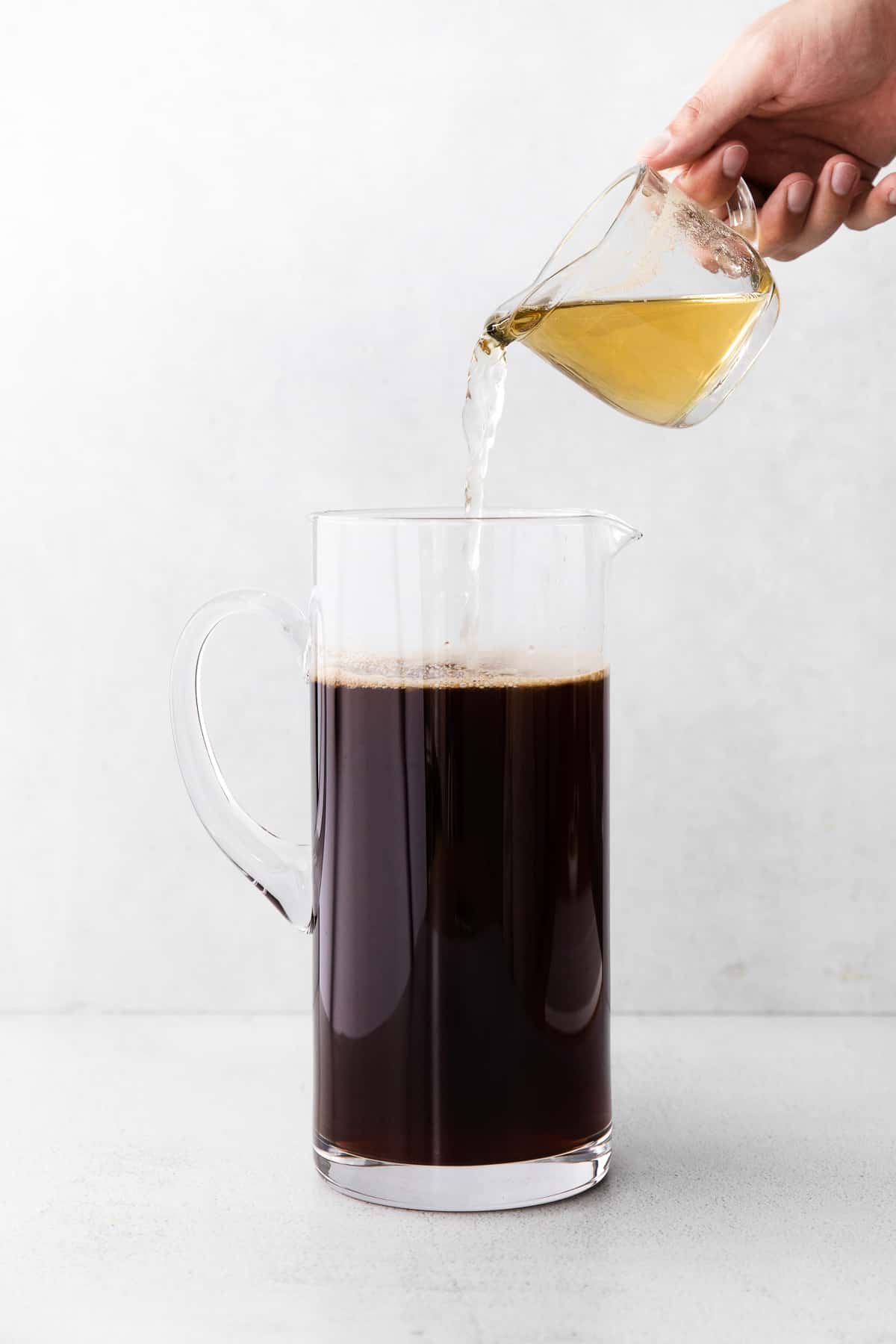 simple syrup being poured into a pitcher of iced tea