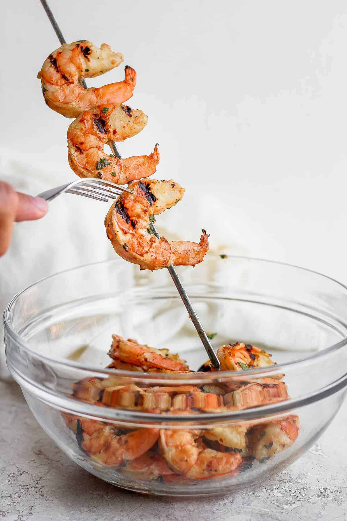 Taking grilled shrimp off skewers and putting them into a bowl.