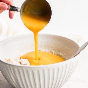 a person pouring orange juice onto peach muffins.