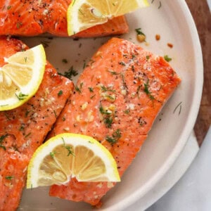 grilled salmon on a white plate with lemon wedges.