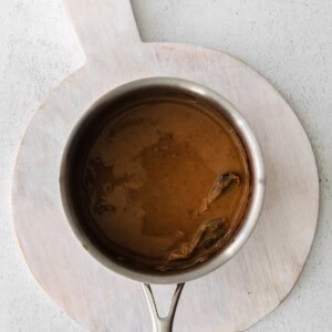 Brown sauce in a pan on a wooden cutting board.