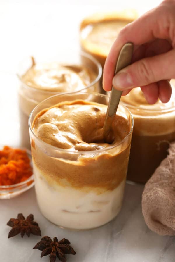 a person pouring a spoonful of peanut butter into a cup.