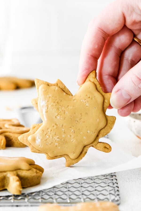 A hand holding a maple leaf cookie on a baking sheet.