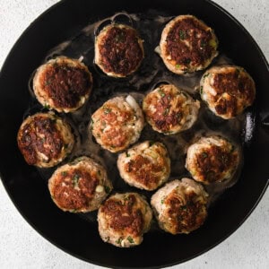 Chicken meatballs in a skillet on a white background.