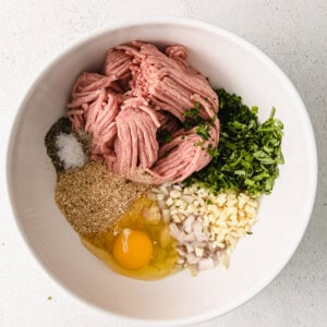 Ingredients for meatballs in a white bowl.