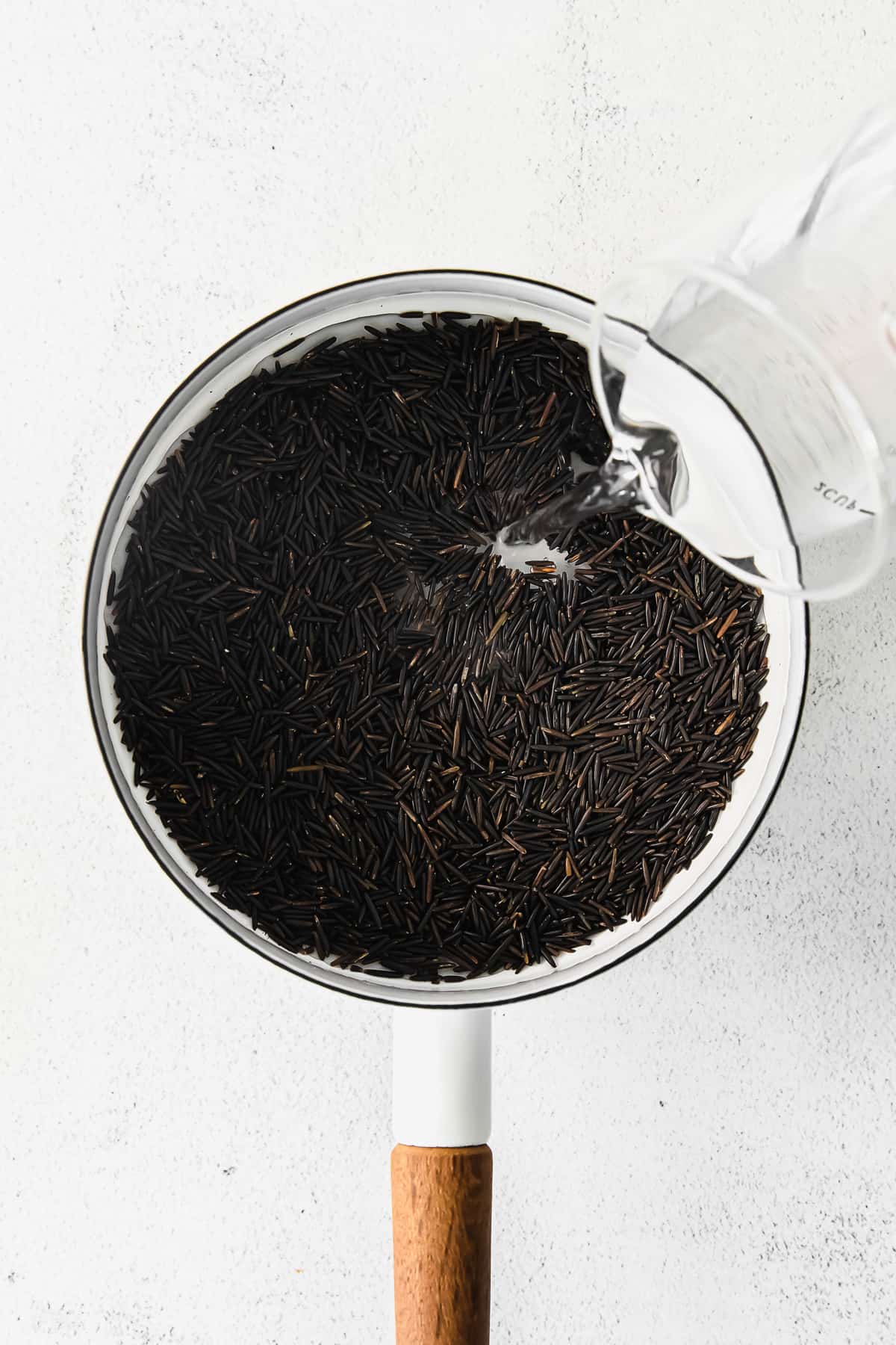 water being poured into a stock pot of dried wild rice