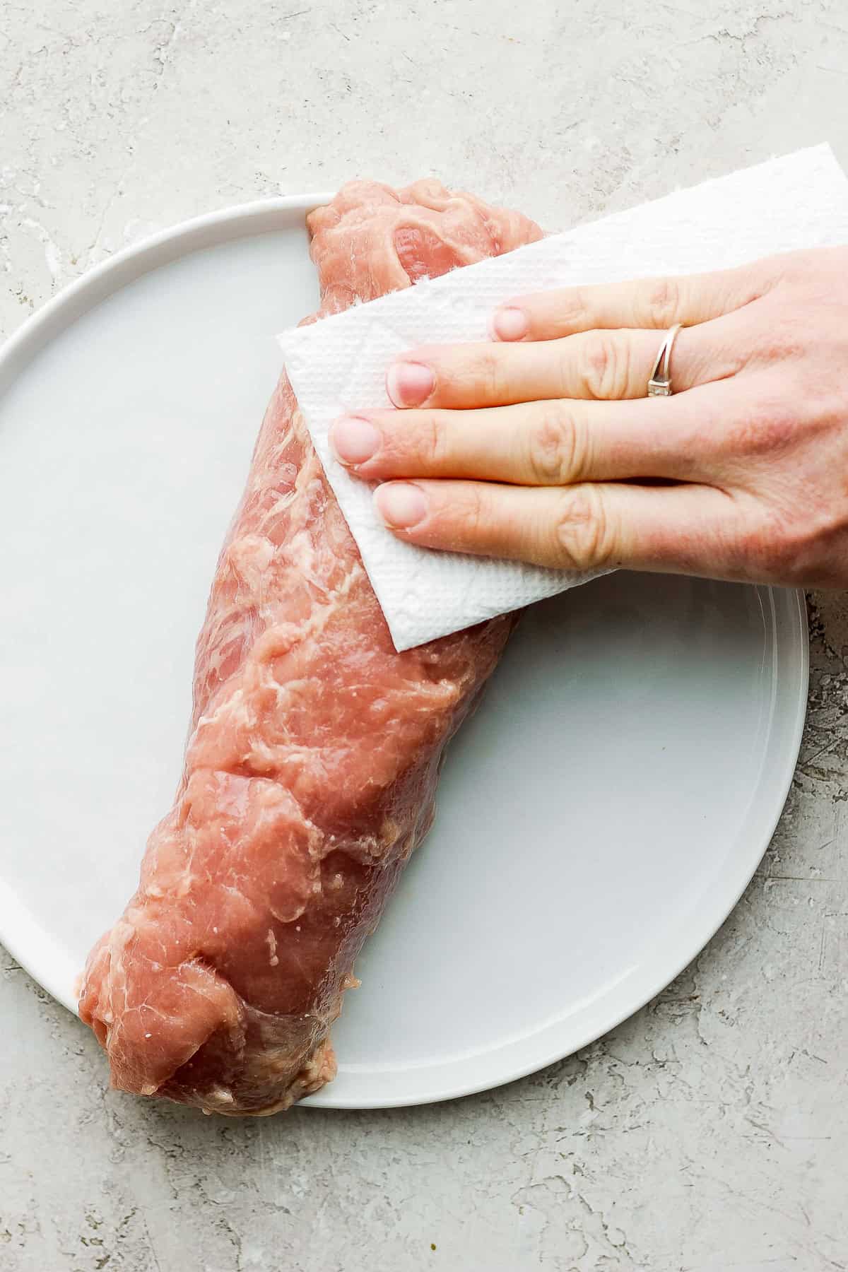 pork tenderloin on a plate being patted dry with a paper towel