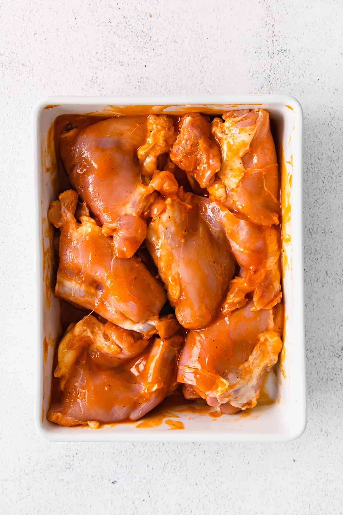 raw boneless chicken thighs in a casserole dish with buffalo sauce