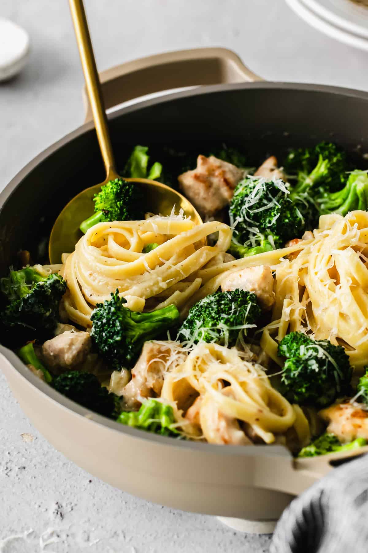 A spoon full of fettuccini noodles and broccoli. 