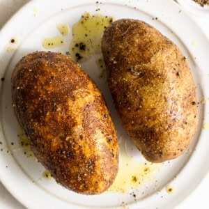 Two roasted potatoes on a white plate.