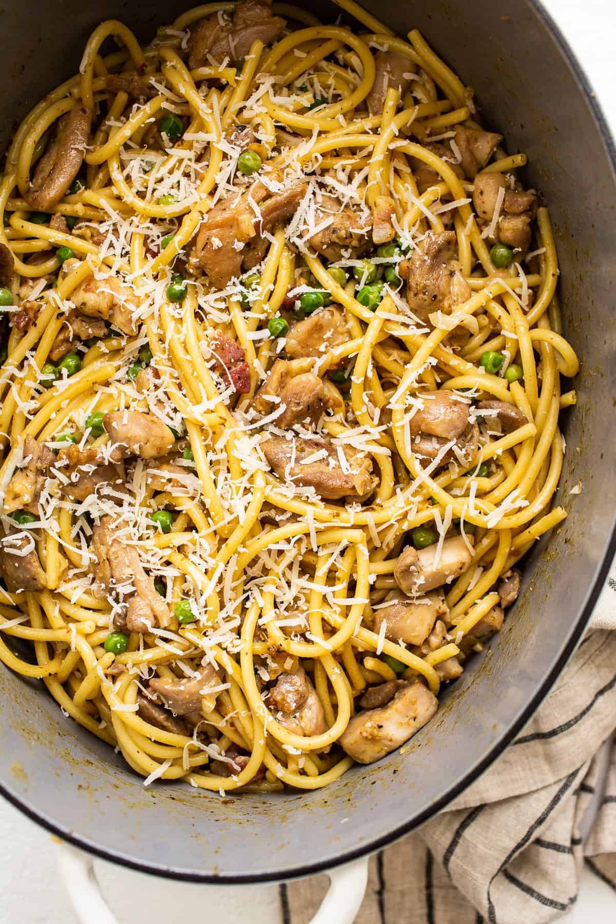 Chicken carbonara in a dutch oven topped with shredded parmesan.