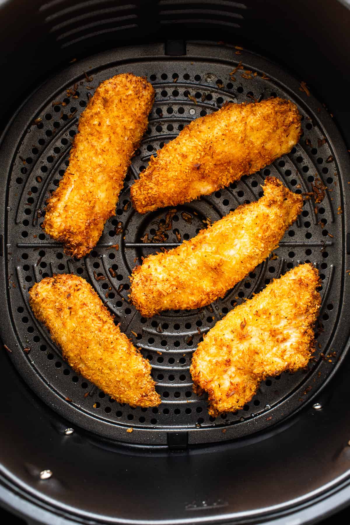 Cooked coconut chicken tenders in an air fryer basket.