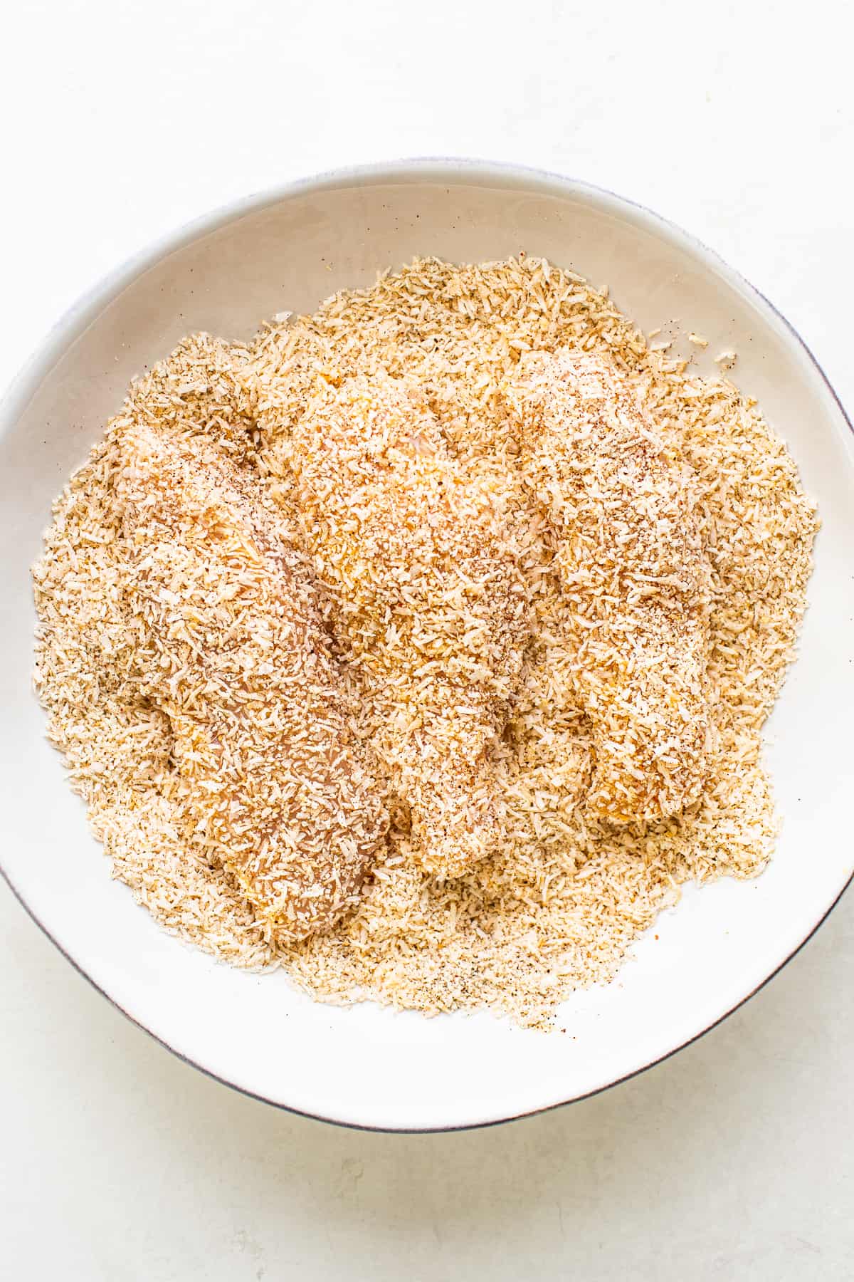 Raw chicken tenders breaded in a bowl.