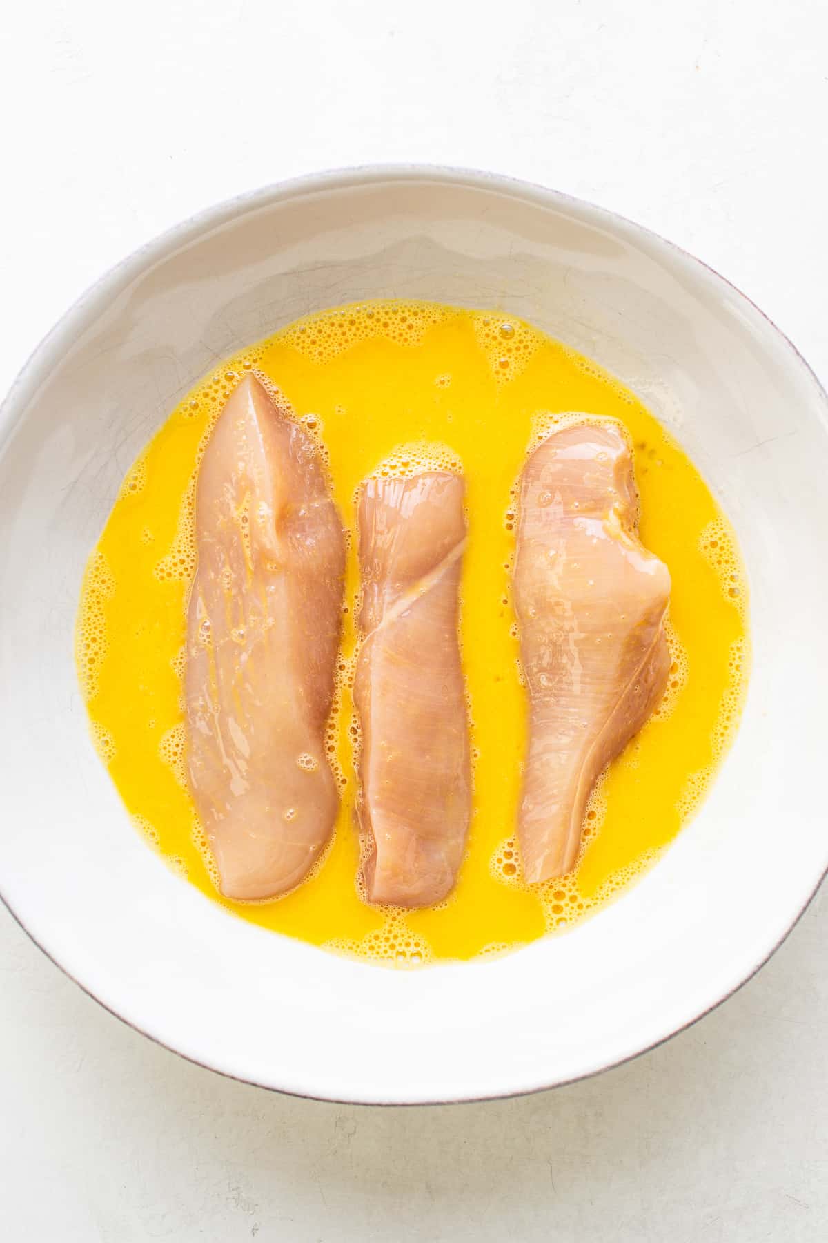 Raw chicken tenders in an egg wash.