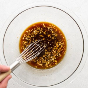 A person whisking an asian sauce in a glass bowl.