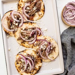 Meat tacos on a baking sheet with onions and limes.