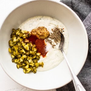 A bowl of yogurt with pickles and a spoon.