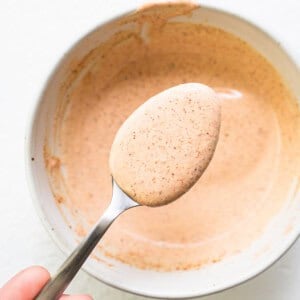 A person holding a spoon full of a brown sauce in a bowl.